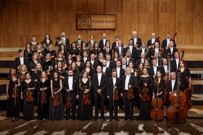 Orkiestra Polskiego Radia, muzycy ubrani w czarne sukienk i fraki stoją w czterech rzędach na estradzie
