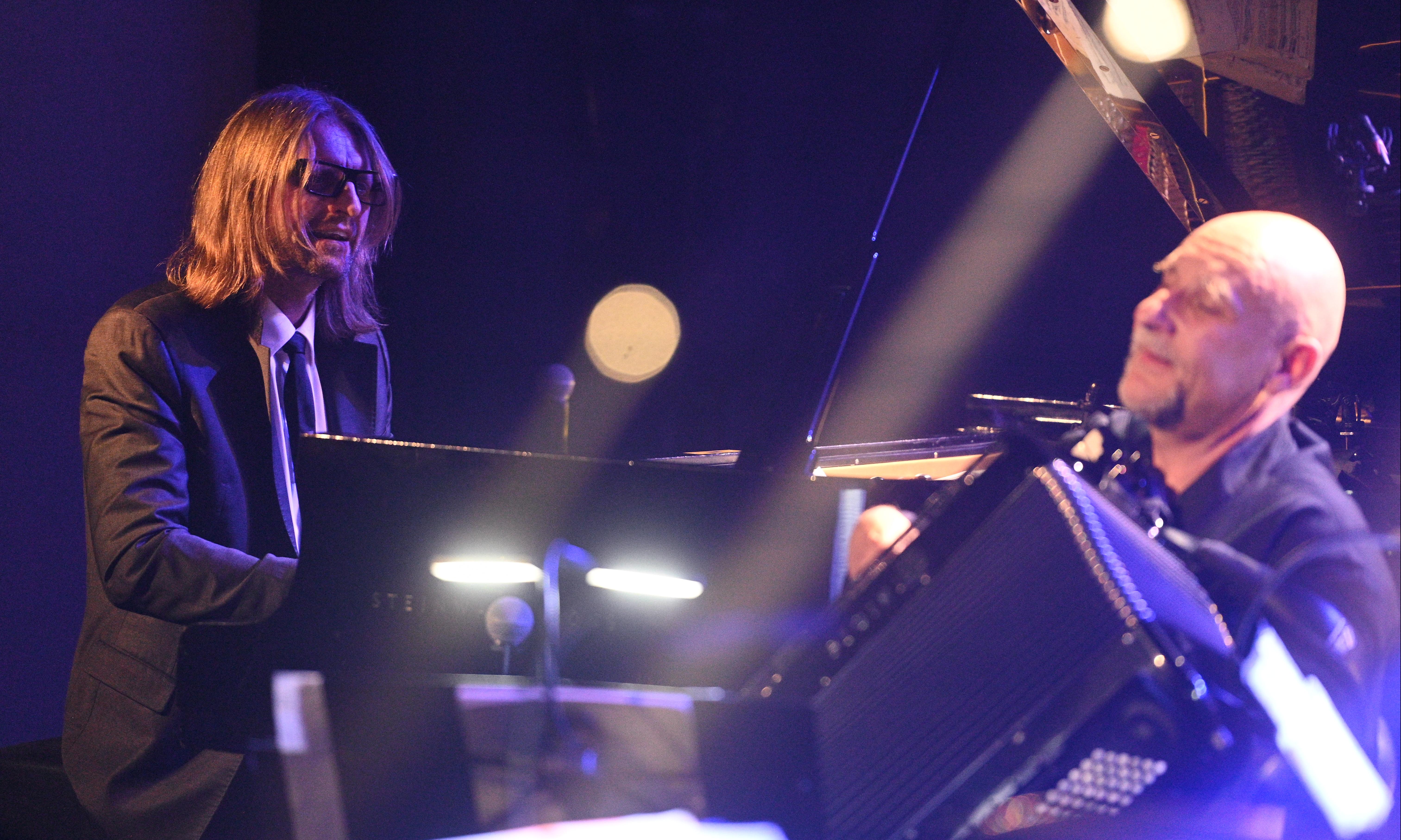 Leszek Możdżer, pianista w garniturze siedzi przy fortepianie, obok gra na aokrdeonie muzyk z Motion Trio Janusz Wojtarowicz